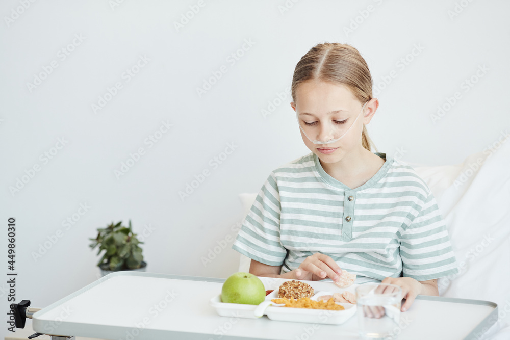 Minimal portrait of girl eating healthy lunch in white hospital room, copy space Minimal portrait of girl eating healthy lunch in white hospital room, copy space