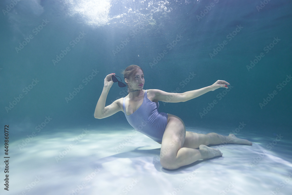 fashion model posing underwater in the pool in a silver swimsuit and sunglasses