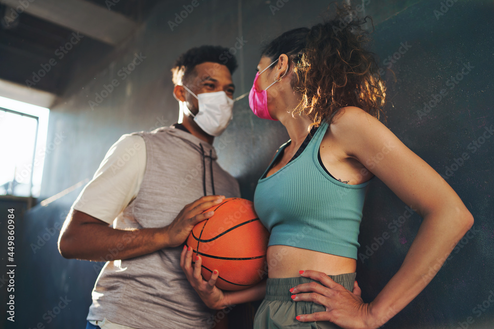 Man and woman friends with basketball doing exercise outdoors in city, talking. Coronavirus concept.