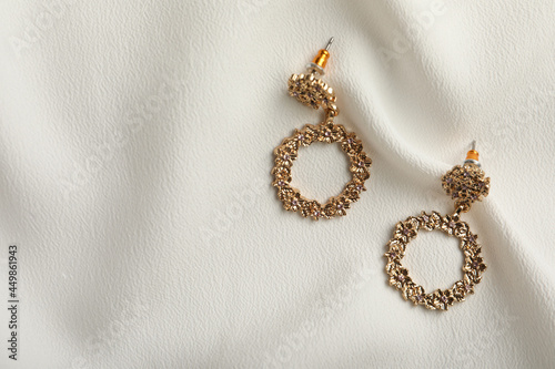 Elegant golden earrings on white fabric, flat lay with space for text. Stylish bijouterie