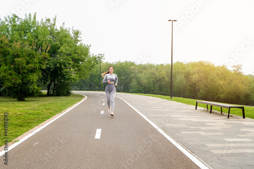 Woman dressed leggings and top running asphalt road summer park. Healthy lifestyle concept. Active and athletic female exercises