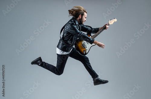 emotional bearded rock musician playing electric guitar in leather jacket and jumping, music