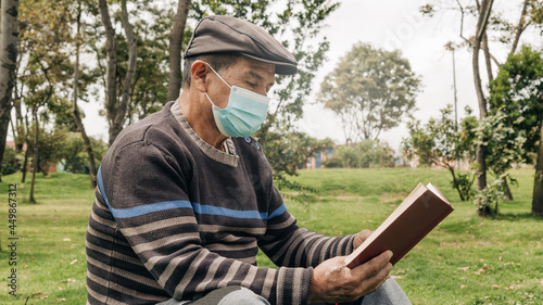 elderly man wearing a face mask to take care of himself, reading quietly in the park