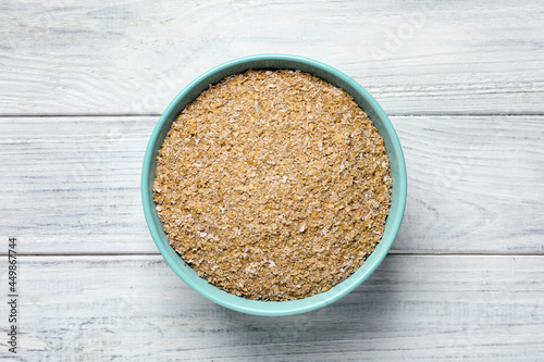 Bowl of wheat bran on white wooden table, top view