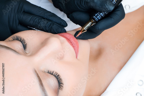 Young woman having permanent makeup on her lips at the beauticians salon