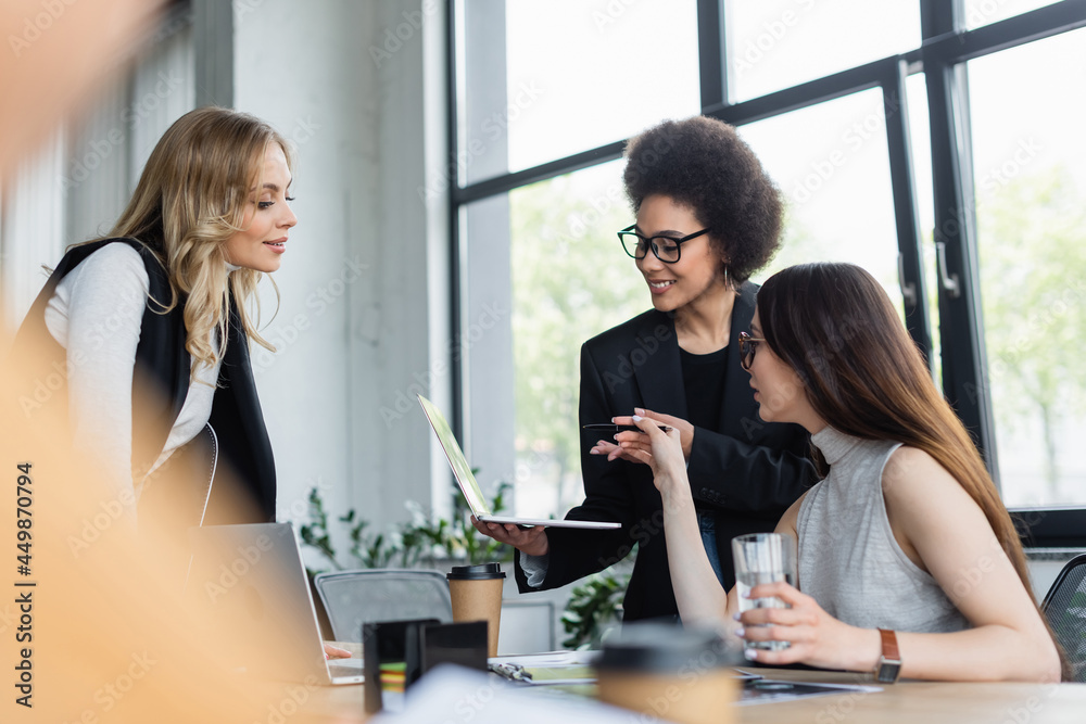 african american and asian managers pointing at laptop near blonde businesswoman african american and asian managers pointing at laptop near blonde businesswoman