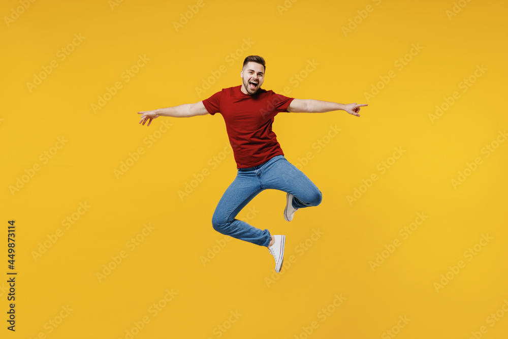 Full length overjoyed fun happy young man wear red t-shirt casual clothes jump high with outstretched hands isolated on plain yellow color wall background studio portrait. People lifestyle concept