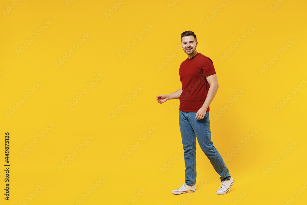 Fototapeta premium Full length smiling happy caucasian young man 20s wear red t-shirt casual clothes walking going look camera isolated on plain yellow color wall background studio portrait. People lifestyle concept