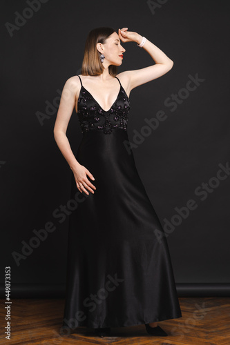 Beautiful woman model dressed in an elegant long black dress in a fashion pose on black background