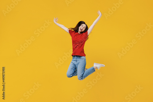 Full size body length excited overjoyed happy young brunette woman 20s wears basic red t-shirt jumping spreading hands isolated on yellow background studio portrait. People emotions lifestyle concept. © ViDi Studio