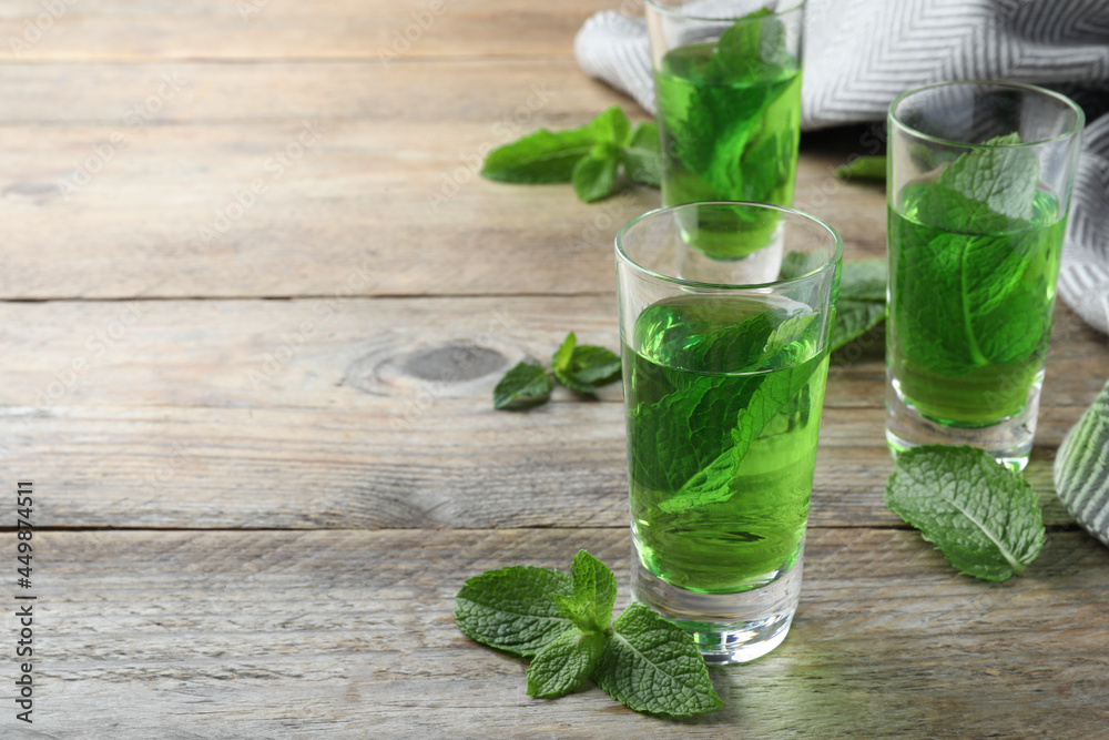 Fototapeta premium Delicious mint liqueur with green leaves on wooden table. Space for text