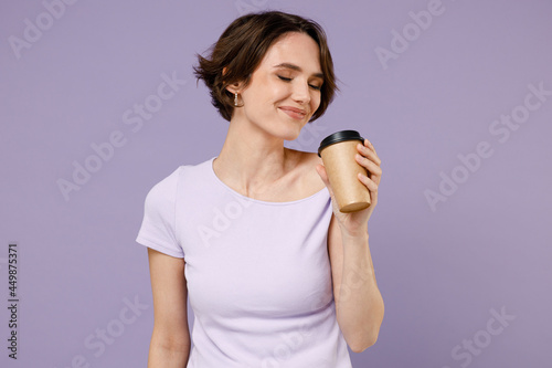 Young fun smiling satisfied happy woman 20s with bob haircut wearing white t-shirt hold takeaway delivery craft paper brown cup coffee to go isolated on pastel purple color background studio portrait