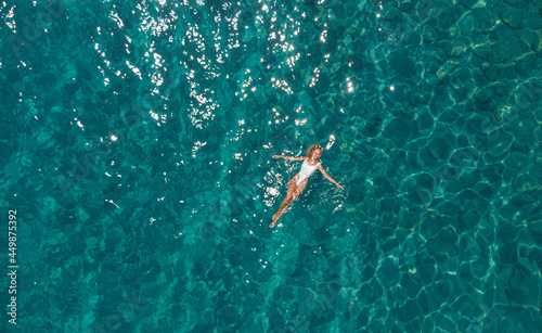 Pretty woman in the white swimsuit swimming in the ocean with clear turquoise water drone photo.