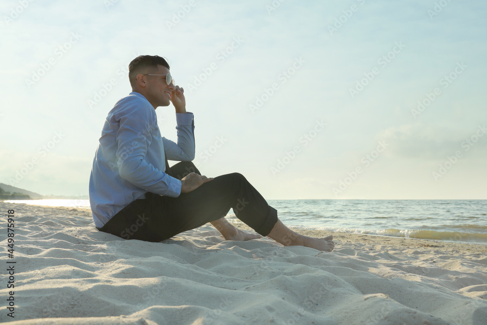 Happy businessman sitting on sandy beach. Business trip
