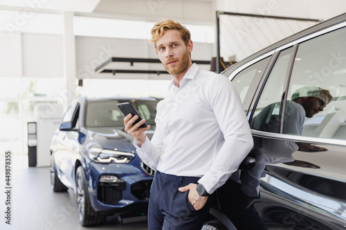 Man pensive customer male buyer client wear white shirt talk mobile cell phone leaning on car choose auto want buy new automobile in showroom vehicle dealership store motor show indoor Sales concept.