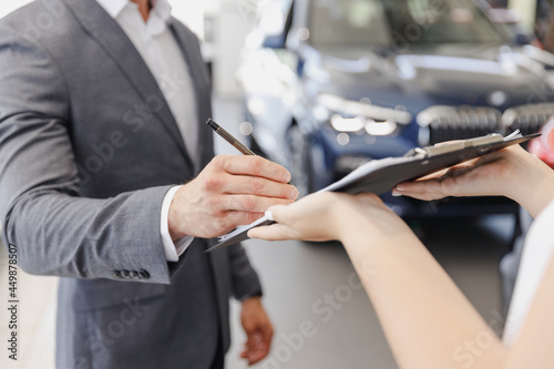 Cropped up photo man customer male client buyer in suit choose auto want buy new car automobile consult with salesman sign document in showroom salon dealership store motor show indoor Sale concept.