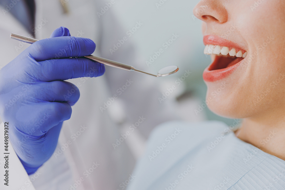 Close up cropped doctor in blue sterile gloves make oral teeth examination for young patient blonde woman sitting at dentist office chair indoor cabinet near stomatologist Healthcare enamel treatment Close up cropped doctor in blue sterile gloves make oral teeth examination for young patient blonde woman sitting at dentist office chair indoor cabinet near stomatologist Healthcare enamel treatment