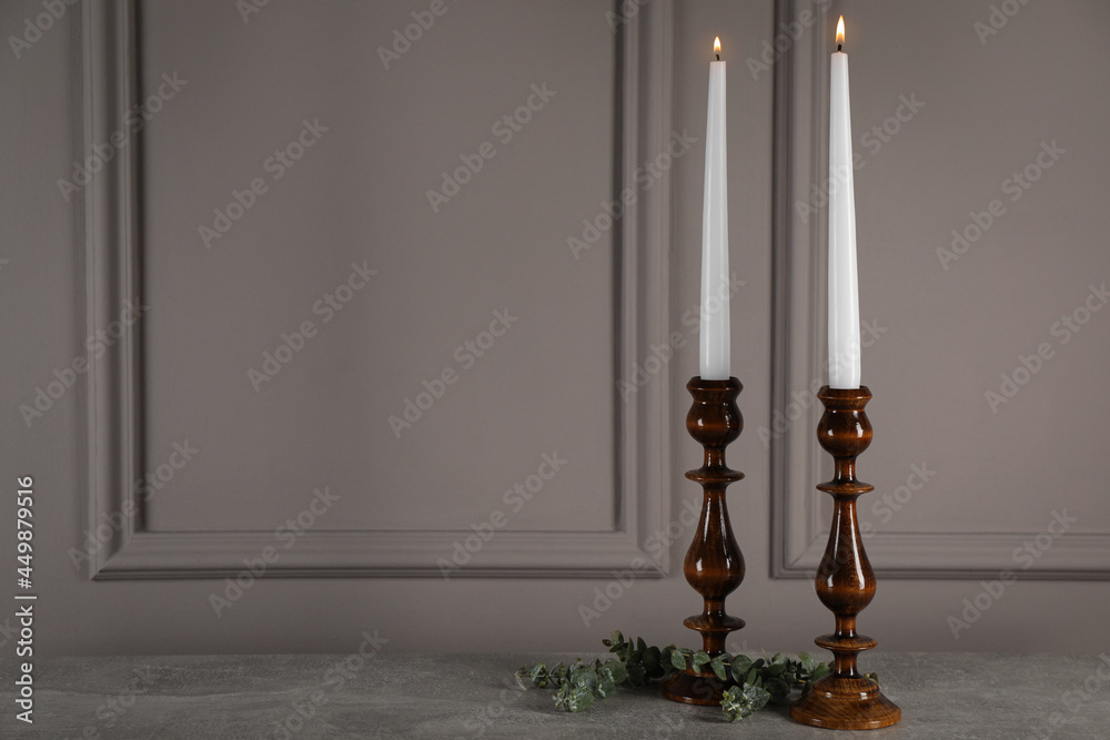 Elegant candlesticks with burning candles and eucalyptus on grey table. Space for text
