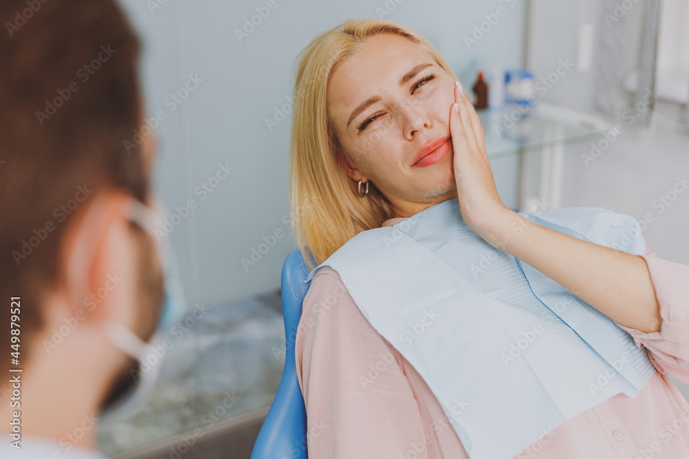 Obraz premium Young sad ill sick woman look at dentist sit at office chair indoor light cabinet hold cheeck visiting stomatologist with toothache painful problem wait cure Healthcare oral enamel caries treatment.