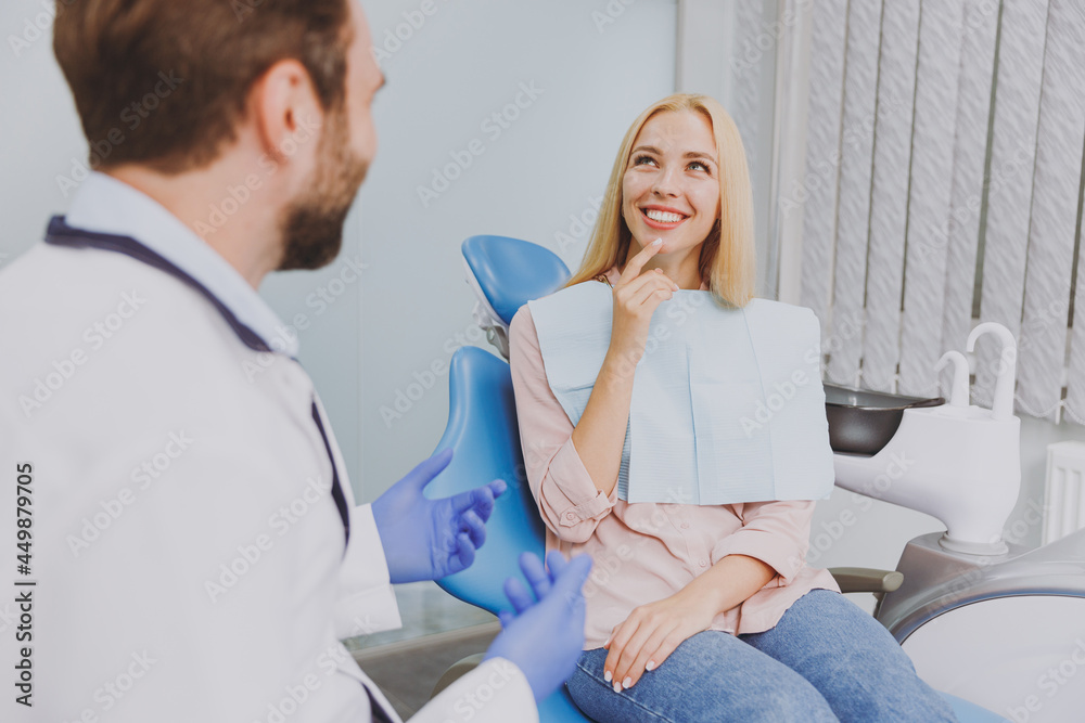 Obraz premium Young man dentist doctor in white gown talk speaking with patient consulting mindedwoman sit at dentist office chair indoor cabinet near stomatologist wait medical cure Healthcare enamel treatment