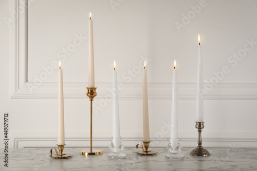 Elegant candlesticks with burning candles on white marble table photo