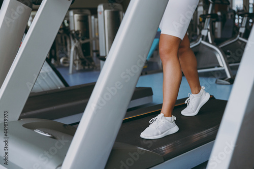Cropped up photo shot young skinny strong sporty athletic sportswoman woman 20s in white sportswear warm up training running on a treadmill in gym indoors. Workout sport motivation lifestyle concept