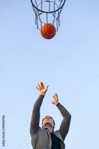 Bottom view cool young sporty strong sportsman man in sports clothes training shooting free throw play with ball at basketball game playground court on sky background Outdoor courtyard sport concept © ViDi Studio