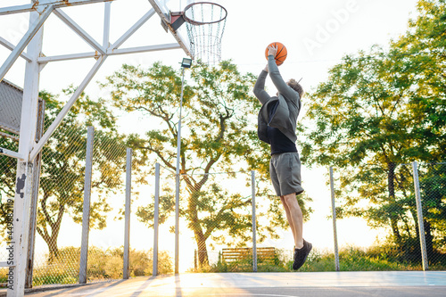 Young side view sporty strong caucasian sportsman man wearing sports clothes training shooting free throw jump playing with ball at basketball game playground court. Outdoor courtyard sport concept © ViDi Studio