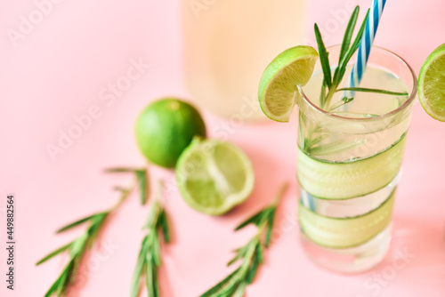 Cold refreshing cocktail with lime, cucumber, rosemary and ice in glass on pink background