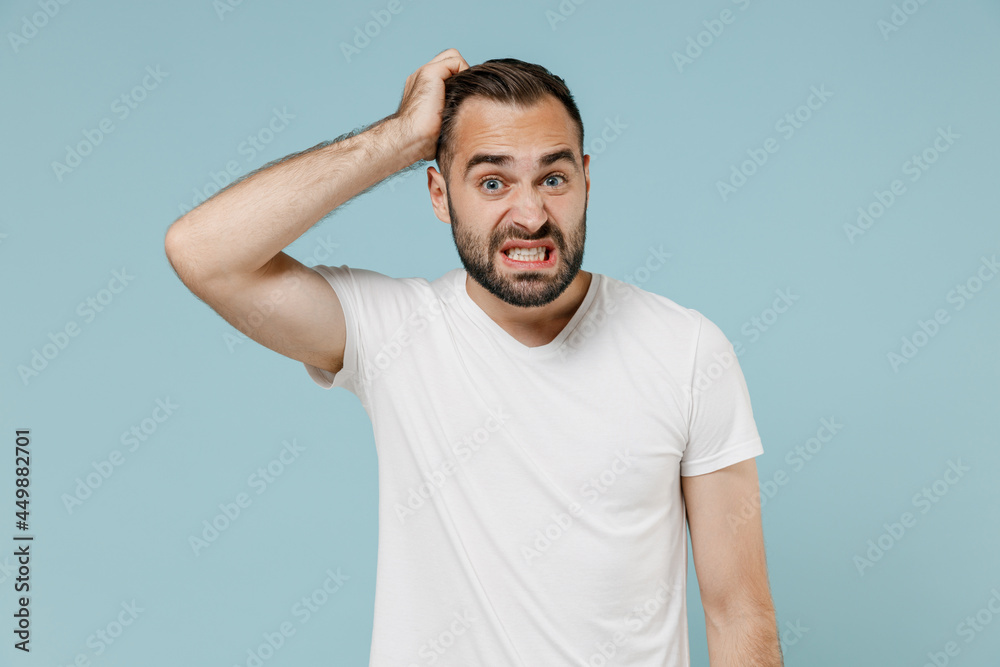 Young confused embarrassed sad puzzled man 20s wearing casual white t-shirt looking camera scratch head isolated on plain pastel light blue color background studio portrait. People lifestyle concept Young confused embarrassed sad puzzled man 20s wearing casual white t-shirt looking camera scratch head isolated on plain pastel light blue color background studio portrait. People lifestyle concept