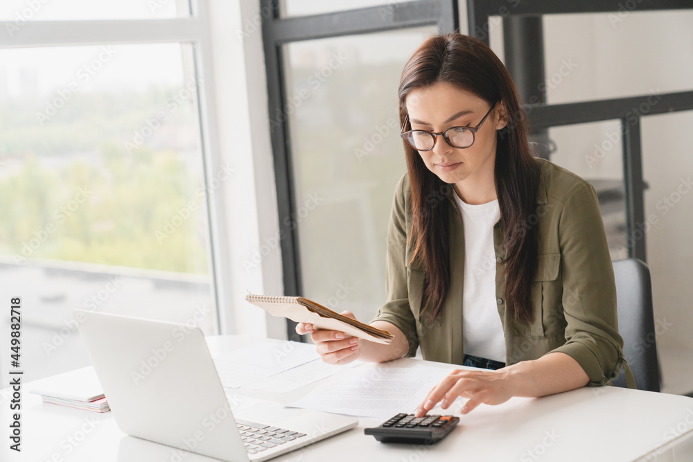 Young caucasian business woman counting funds, planning budget, paying bills online using calculator. Freelancer boss CEO doing paperwork with finances. Young caucasian business woman counting funds, planning budget, paying bills online using calculator. Freelancer boss CEO doing paperwork with finances.
