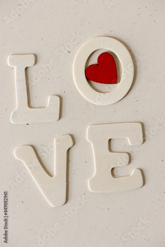 the word "love" in plain wooden letters on a neutral paper background - with a red heart