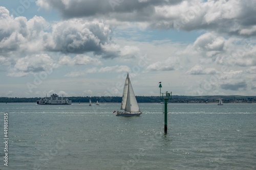 yacht sailing towards a seaside sentry a coastal navigation marker with a ferry and the Isle of Wight Hampshire England in the background