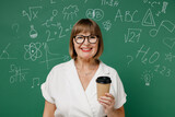 Smiling cheerful clever fun teacher mature elderly lady woman 55 wear shirt glasses hold takeaway delivery craft paper brown cup coffee to go isolated on green wall chalk blackboard background studio.
