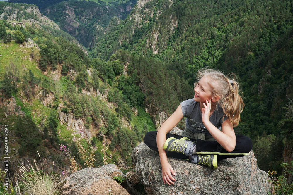 Young girl sitting at edge of cliff looking over expansive view of plains and mountains