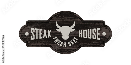 Colored illustration of a bull's head, text on a background with a wooden texture. Design element for signboard, banner, emblem, label. Vector illustration. Steak house advertisement.