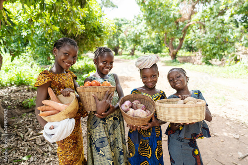 Group of pretty smiling African girls carrying baskets full of vegetables, on their way to the lokal market photo