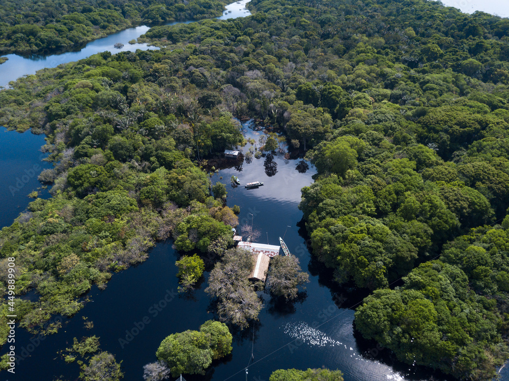 Drone aerial view of forest trees, small houses and boats in the biggest flood of the Negro river history in the Amazon rainforest. Concept of environment, ecology, climate change, global warming.