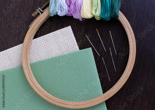 The mouline thread and a wooden round hoop lie on the fabric for embroidery with a counted cross. photo