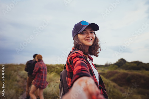 Come with me. Beautiful girl holding man by hand and walking down the mountain valley looks and smiles at camera. Active lifestyle, friendship, care, ecology concept