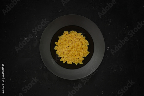 Raw pasta farfalle on plate on black background. Top view of Italian cuisine ingredient.