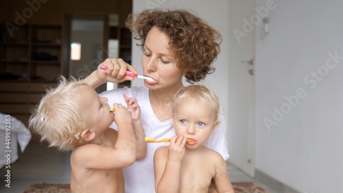 Young mom teaches her twin babies how to brush teeth. Hygiene rituals as a bonding quality time