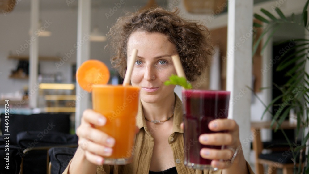 Blonde girl showing to the camera glasses of natural organic carrot and beetroot juices with paper straws. Plant based cold refreshing drinks. Blonde girl showing to the camera glasses of natural organic carrot and beetroot juices with paper straws. Plant based cold refreshing drinks.