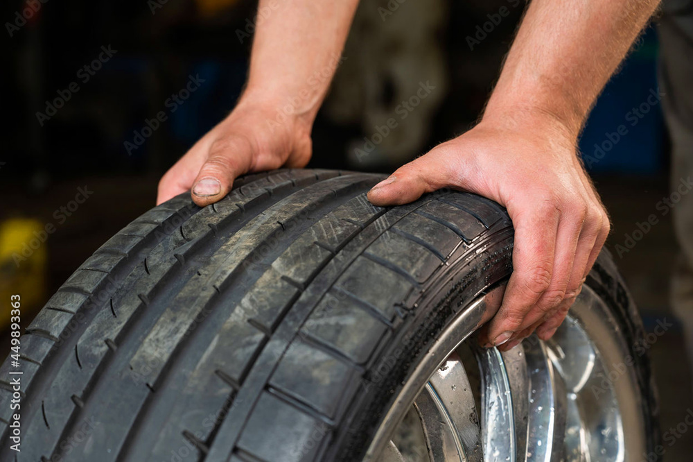 Obraz premium auto mechanic holds a wheel of a car. Change of car tires acc