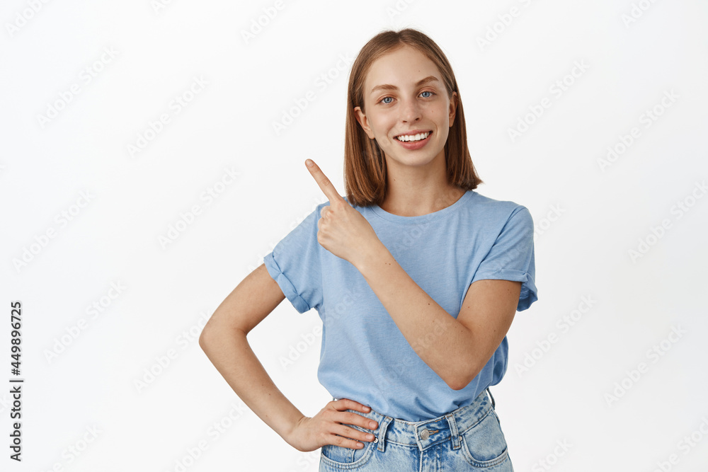 Obraz premium Image of satisfied, smiling happy girl pointing at upper left corner sale logo, showing advertisement, recommending store, standing in t-shirt over white background
