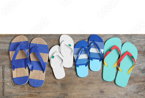 Pairs of bright flip flops on wooden table against white background, top view