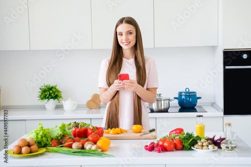 Photo portrait young woman cooking vegetables using smartphone at home