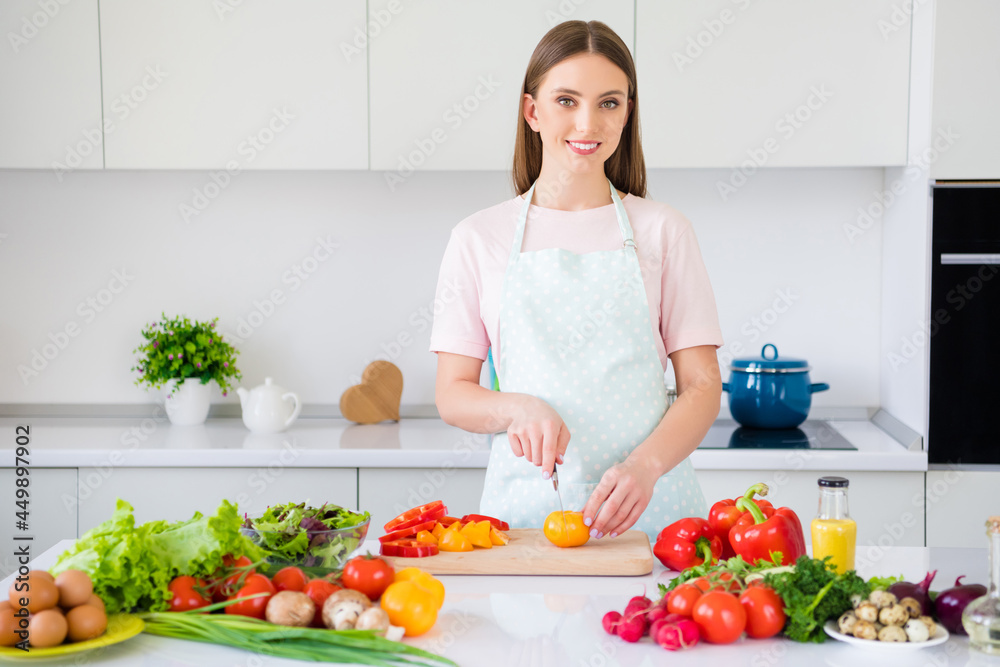 Portrait of attractive cheerful girl cutting tomato cooking fresh meal organic bio product at home light white kitchen indoors