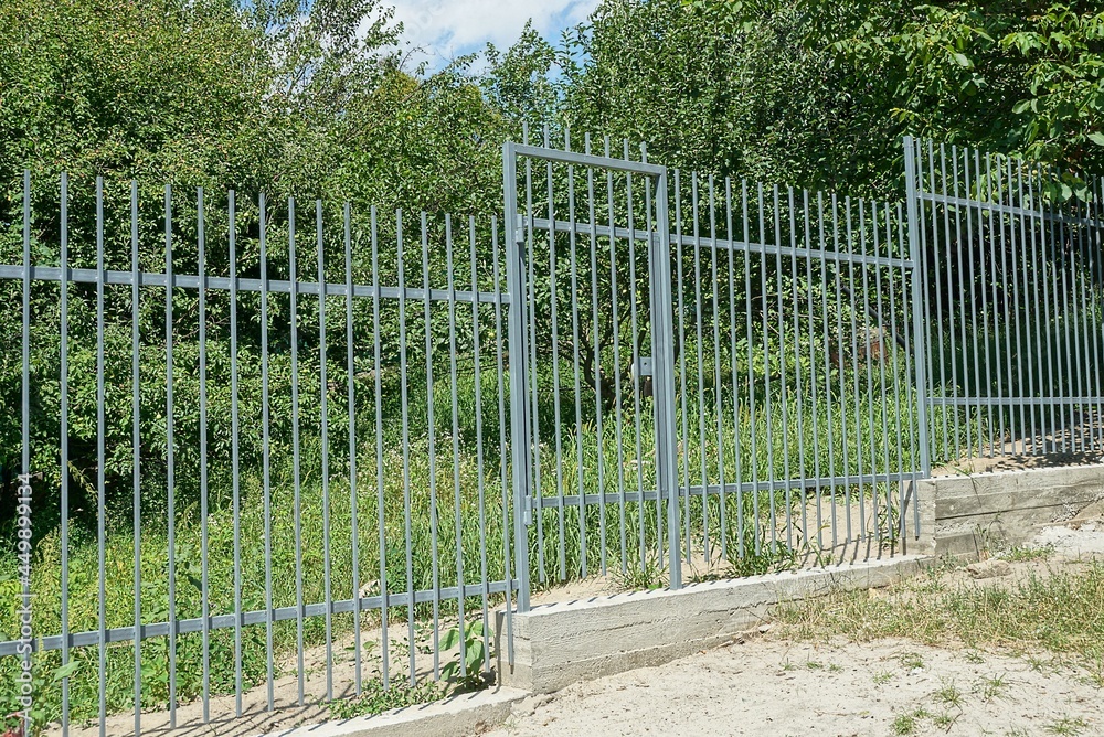 part of a gray metal wall of a fence with a closed door made of iron rods on a concrete foundation on the street part of a gray metal wall of a fence with a closed door made of iron rods on a concrete foundation on the street