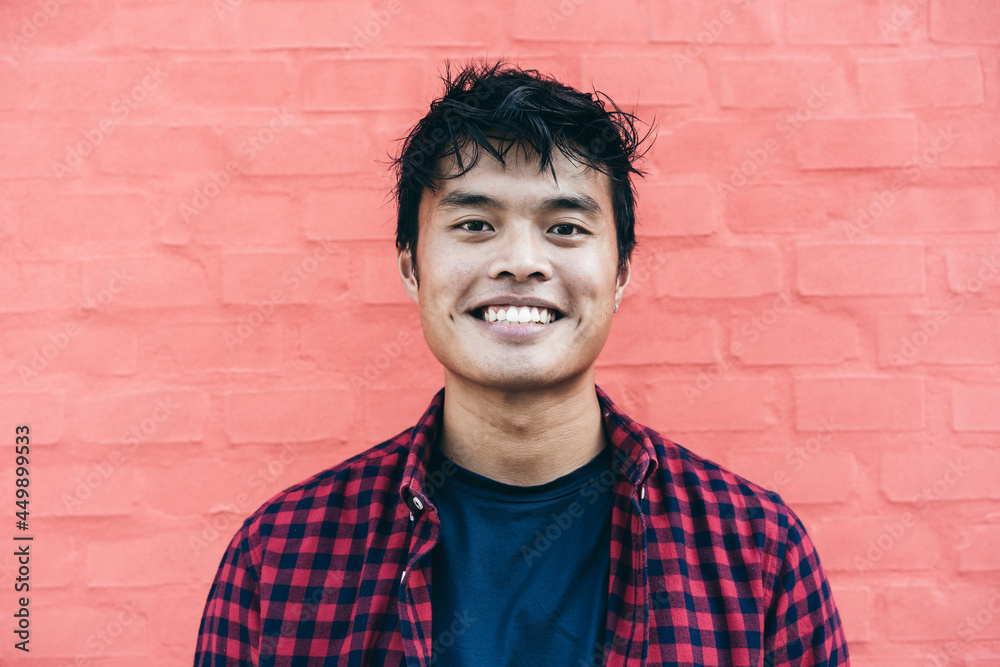 Happy Asian guy portrait - Confident asian young male having fun smiling while posing in front of camera against a red wall background - obrazy, fototapety, plakaty 